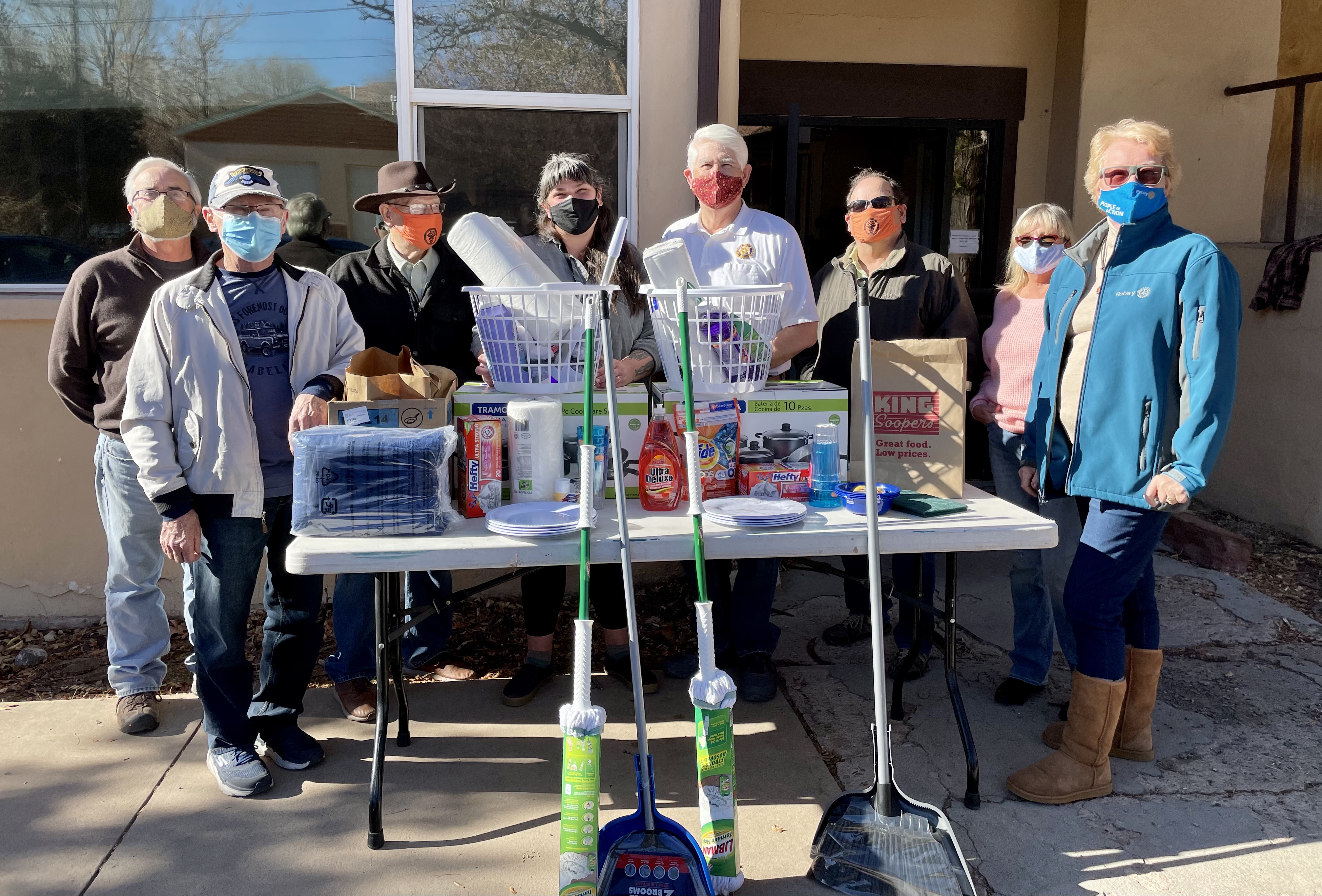 people standing next to and behind a table with cleaning, kitchen, and other household supplies