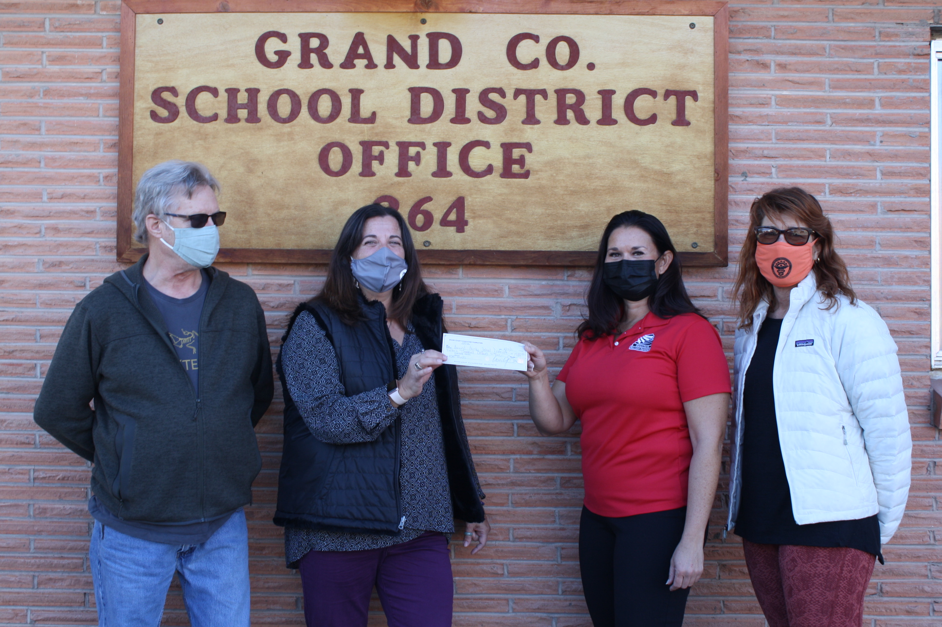 Photo of four people wearing masks, with the middle two holding a check together