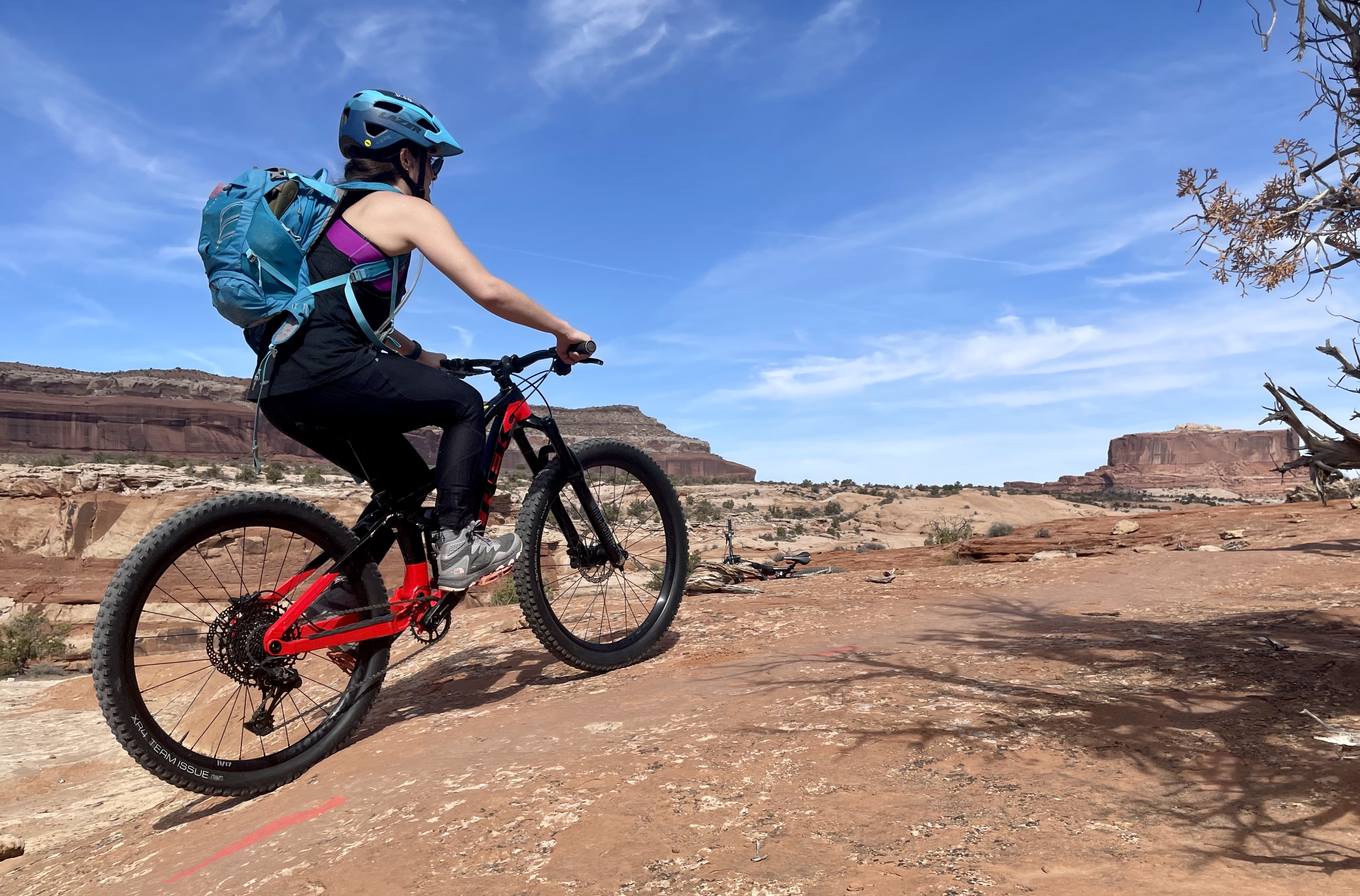 A woman biker rides up a slope, with a pair of sheer cliffs as a backdrop