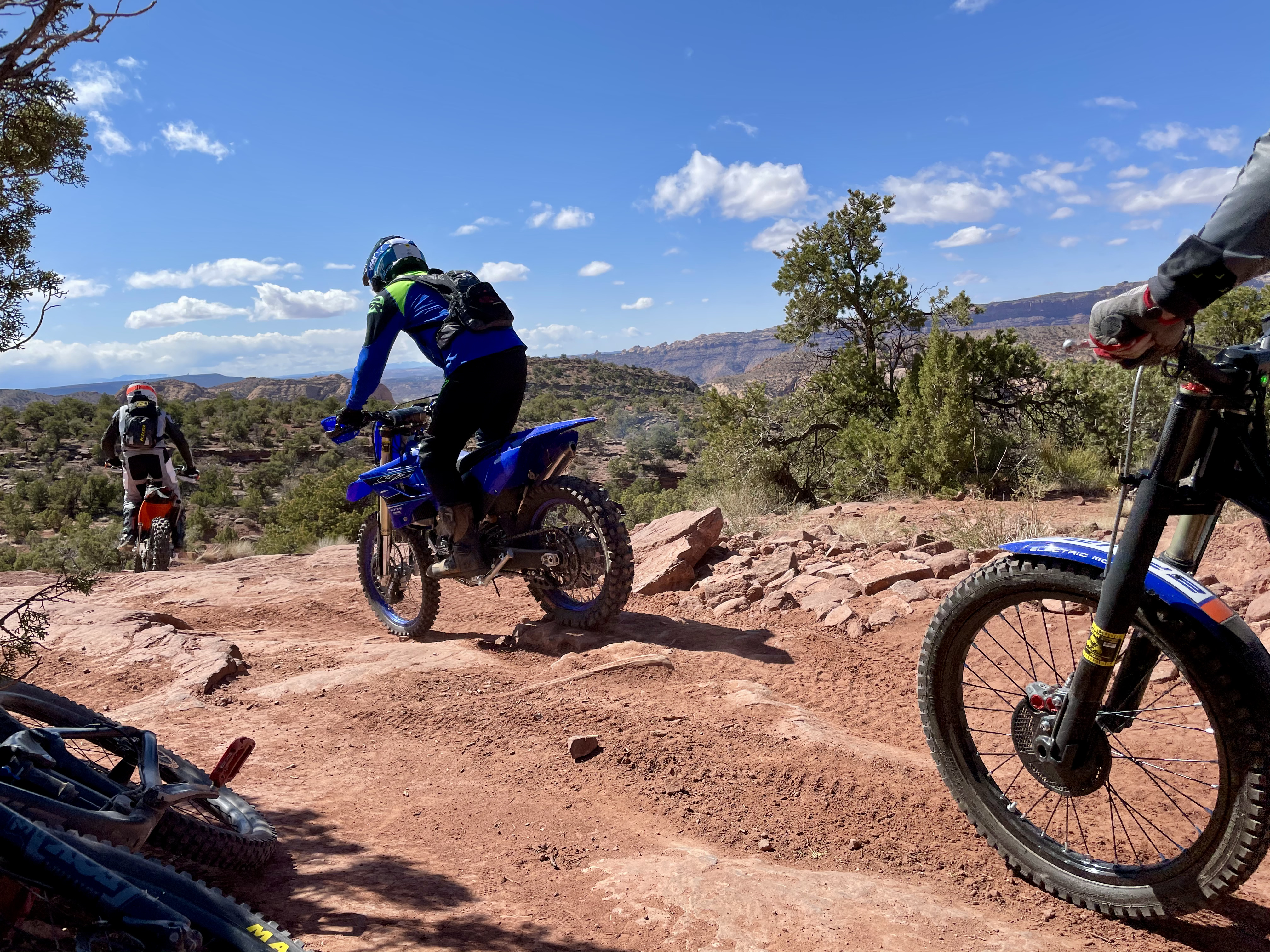 three dirt bikers ride left, away from the viewer, with a mountain bike laying down, next to the viewer