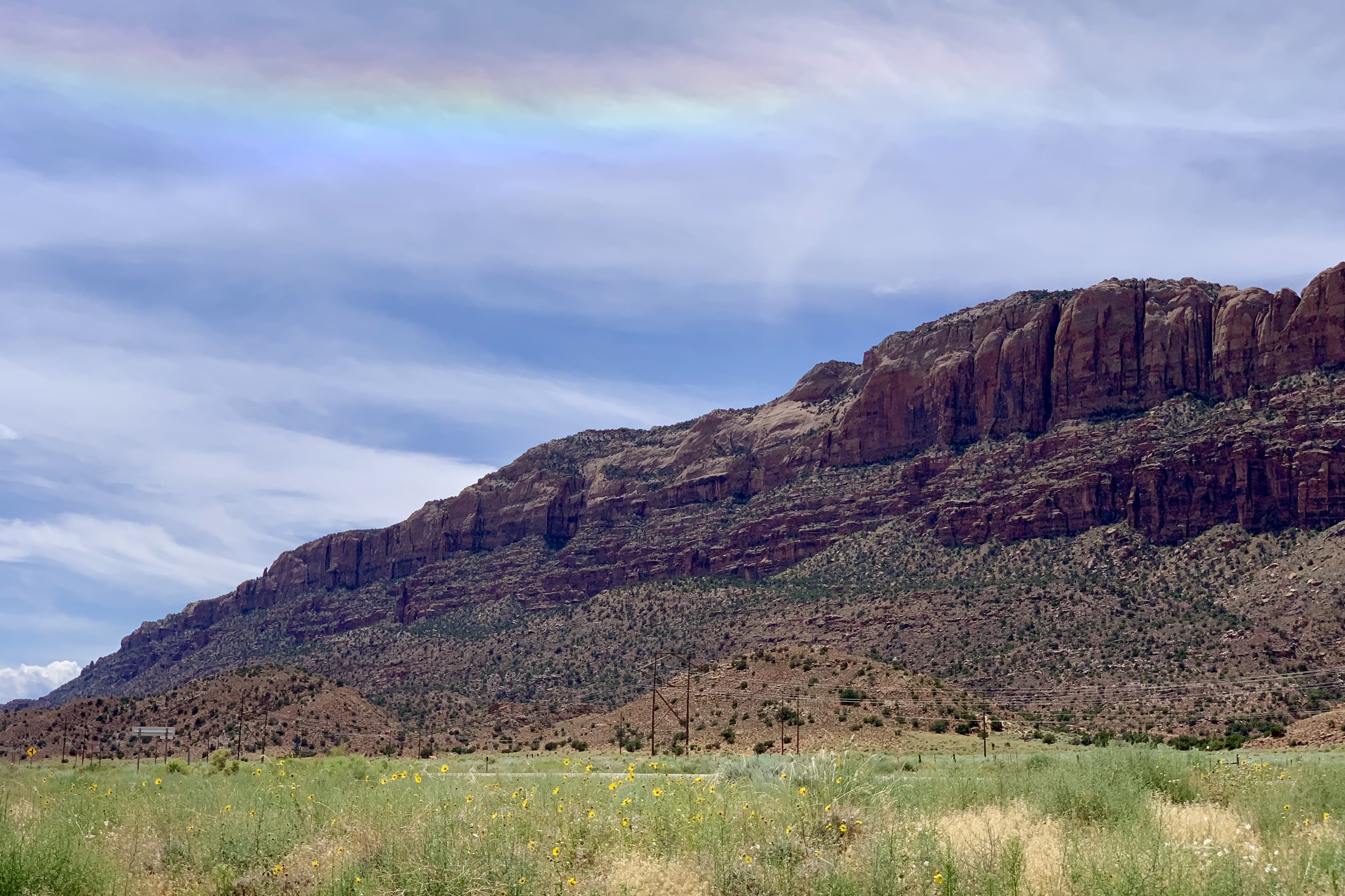 a rainbow appears over the western rim of Moab, which is photographed sloping down to the south, which is left in the photo