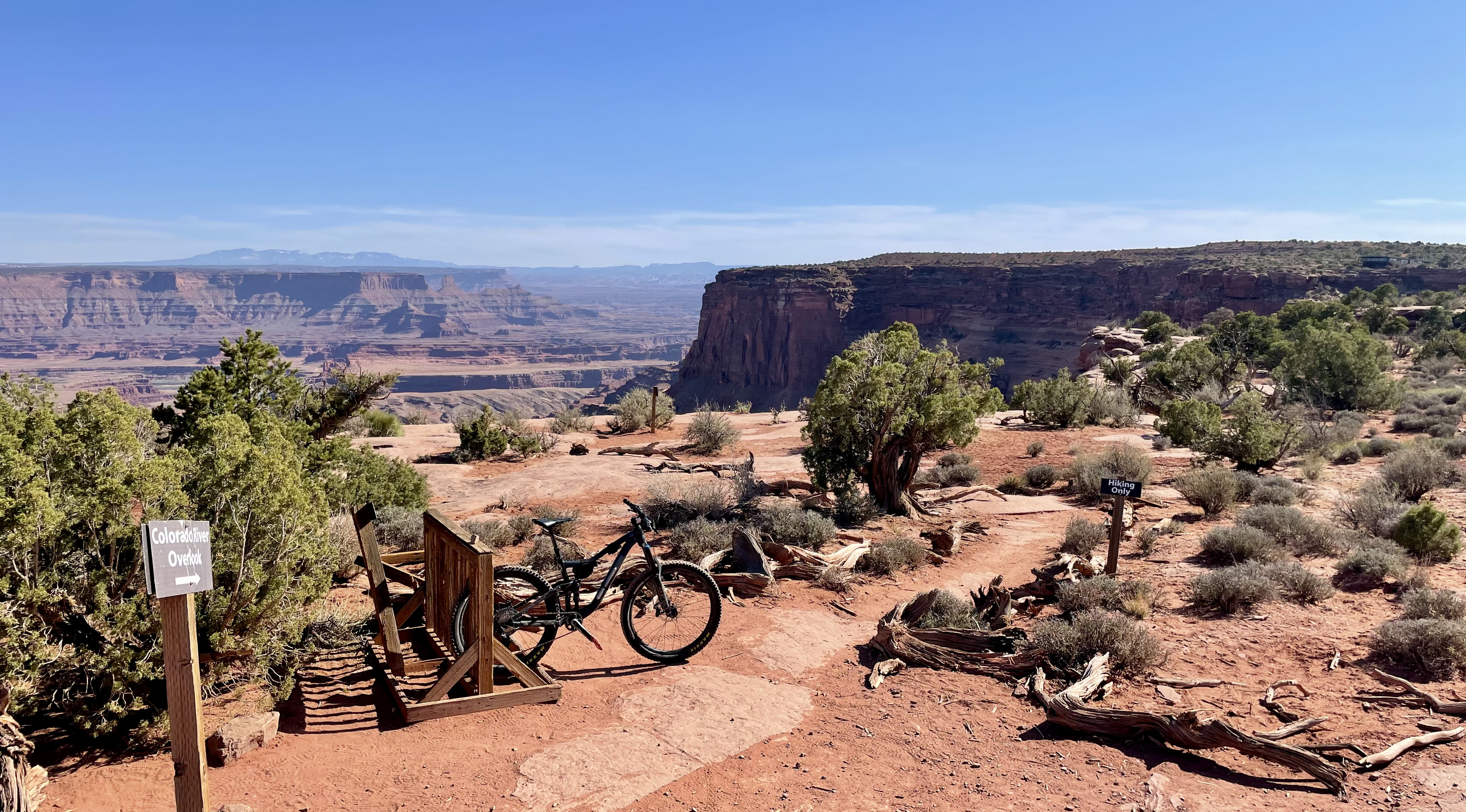 A bike rack at left with my bike, next to a sign that reads "Colorado River Overlook." Another sign reads "Hiking Only" on the way to the ledge.