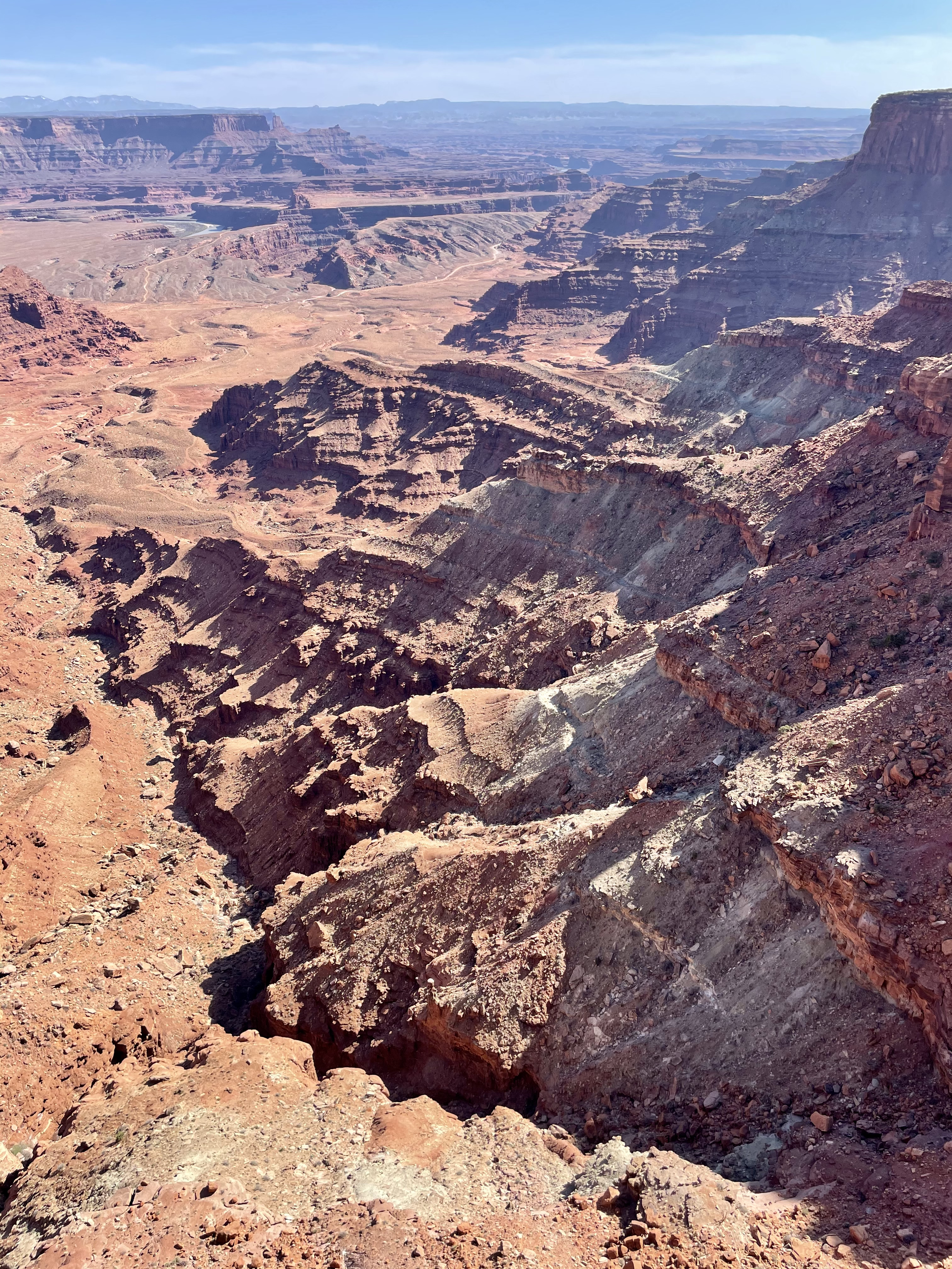 Red rocks, textured with afternoon shadows and layers of varying rock groups, sit between the viewer and the Colorado River, barely visible at the bottom of a distant canyon.