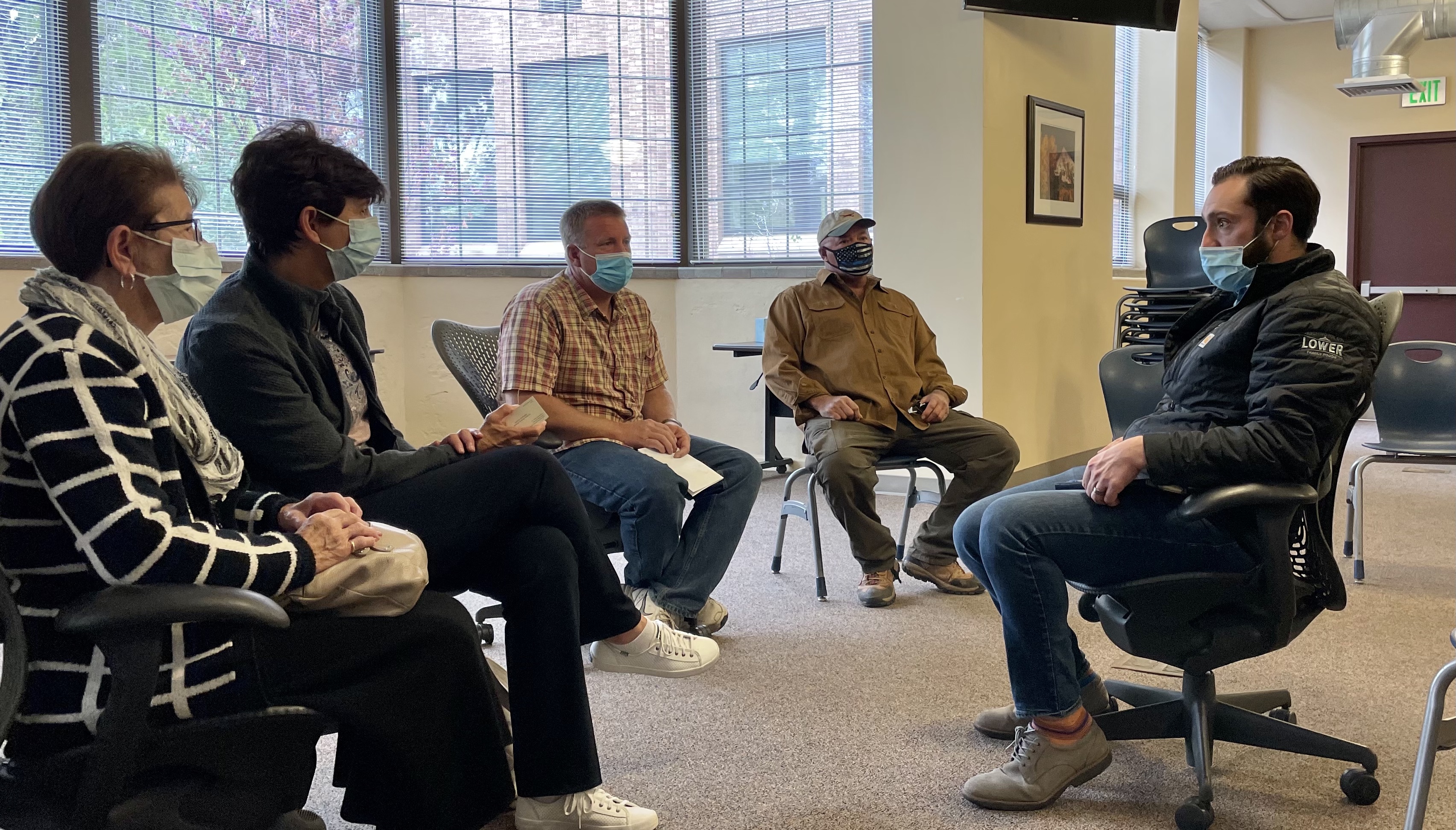 Four people at left wearing respiratory masks face a man at right, also masked, as he leans in to speak.