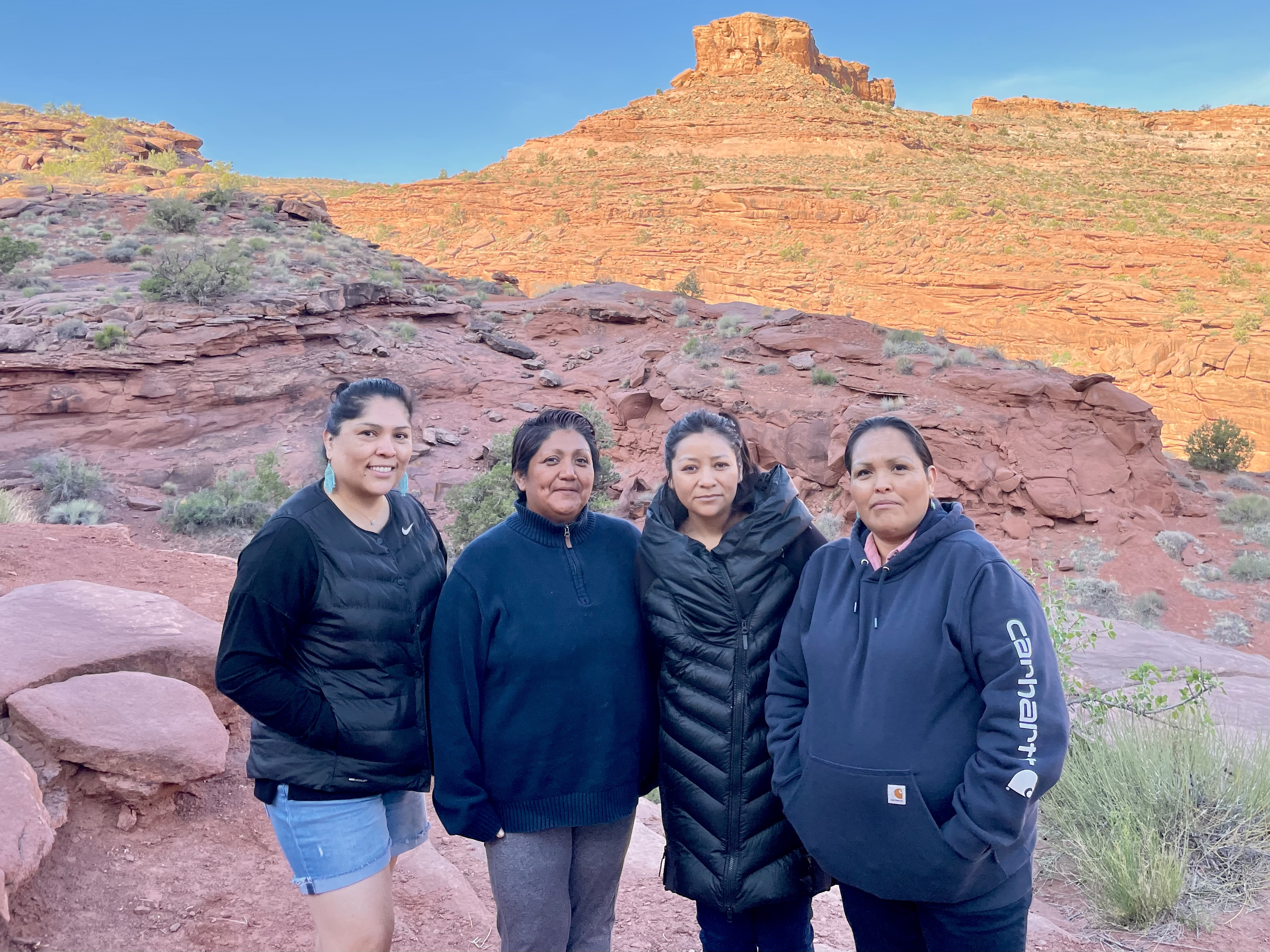 four women, all mothers, stand in front of red rock scenery near Birthing Rock in Moab, Utah
