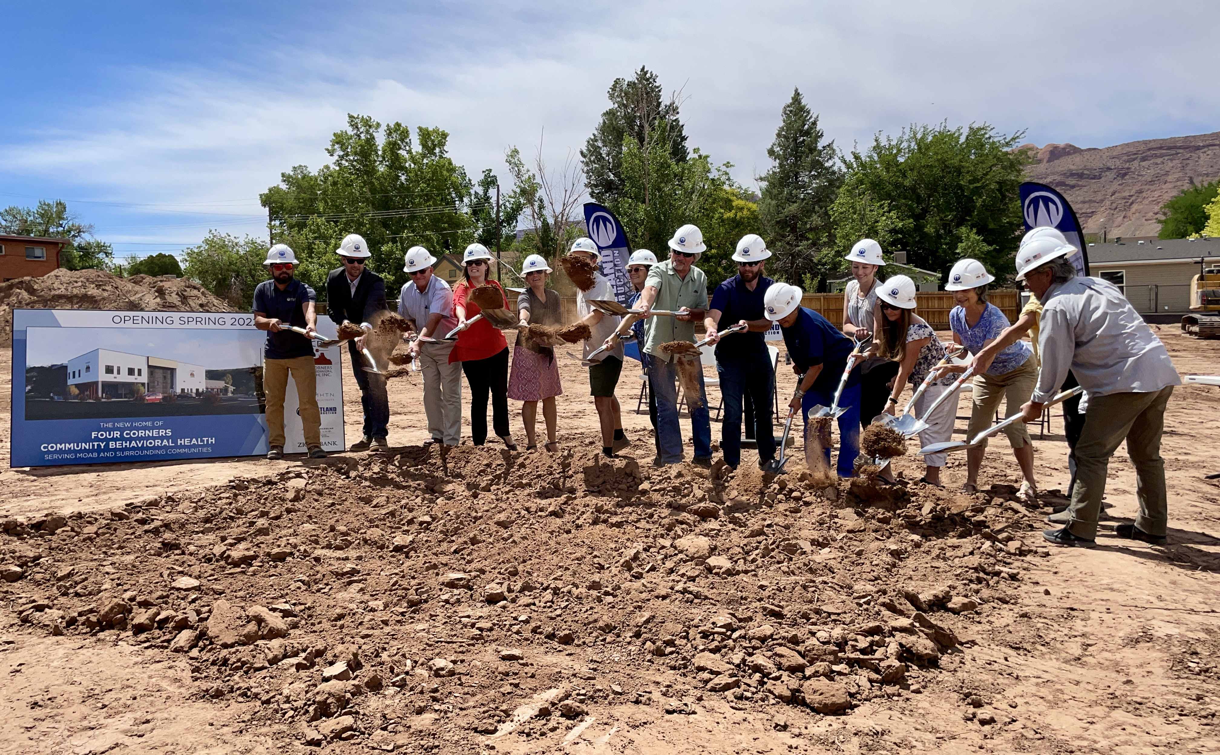 well-dressed people wearing hard hats shovel dirt in a ceremonial groundbreaking