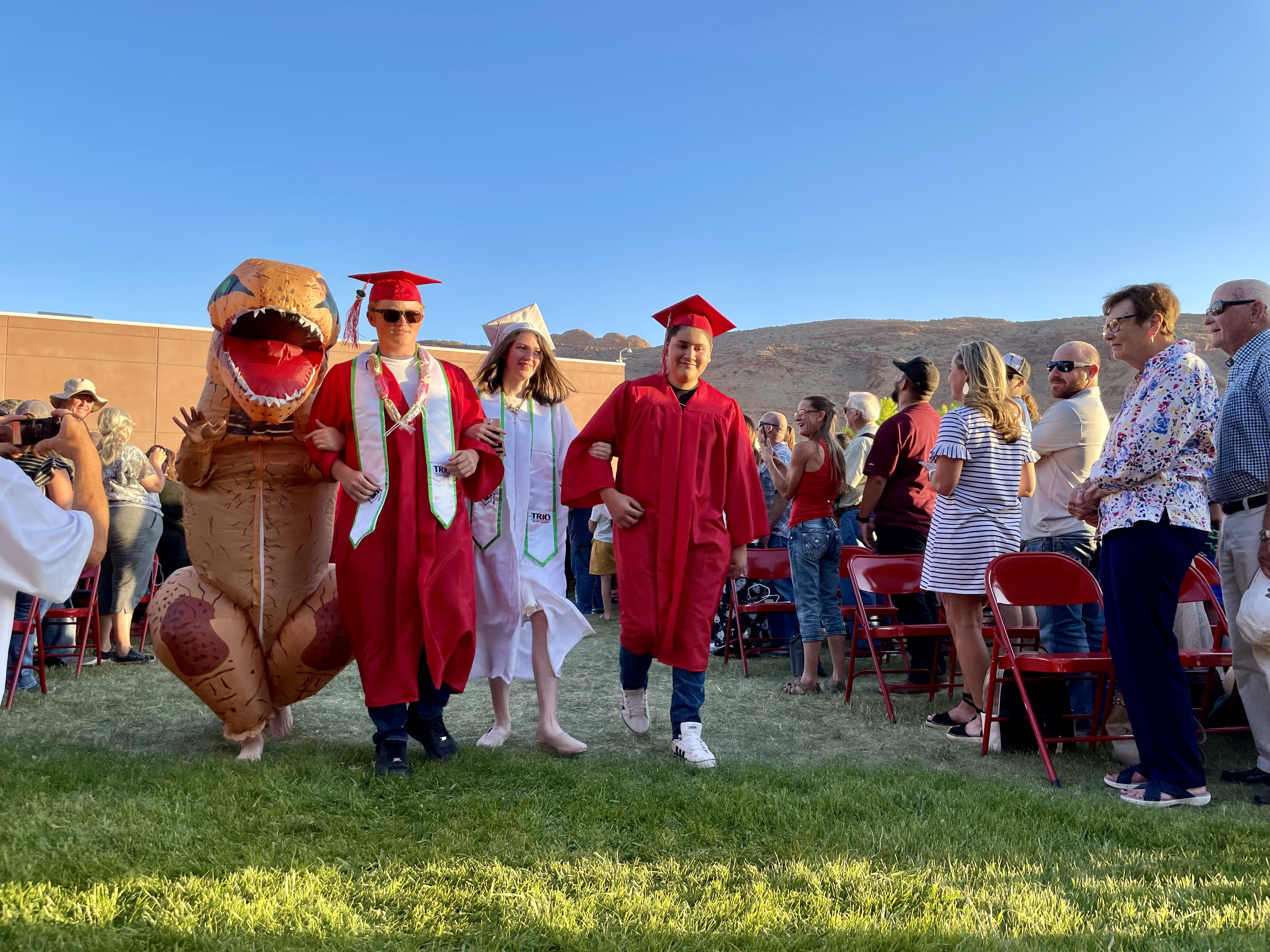 Three Grand County High School students and a dinosaur walk down the grassy aisle during the Class of 2021’s graduation ceremony. 
